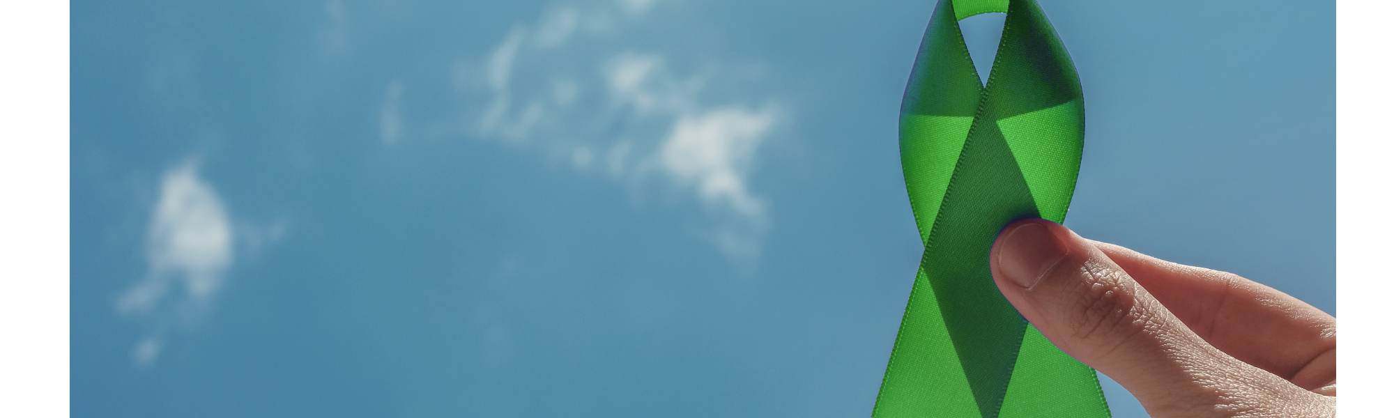 Hand holding a green awareness ribbon symbolizing mental health awareness against a blue sky