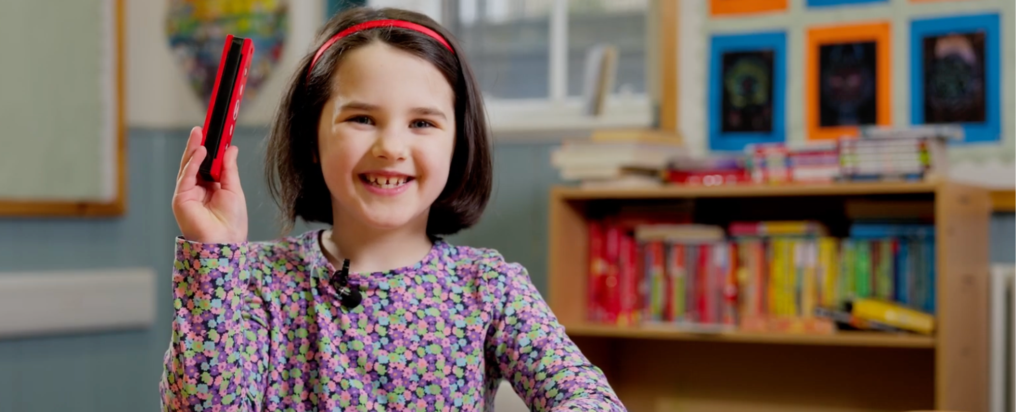 Girl in a classroom, raising her hand and smiling at the camera