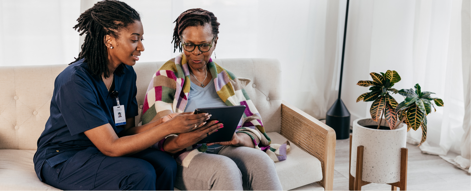 A nurse and patient sitting in a sofa, looking at a tablet