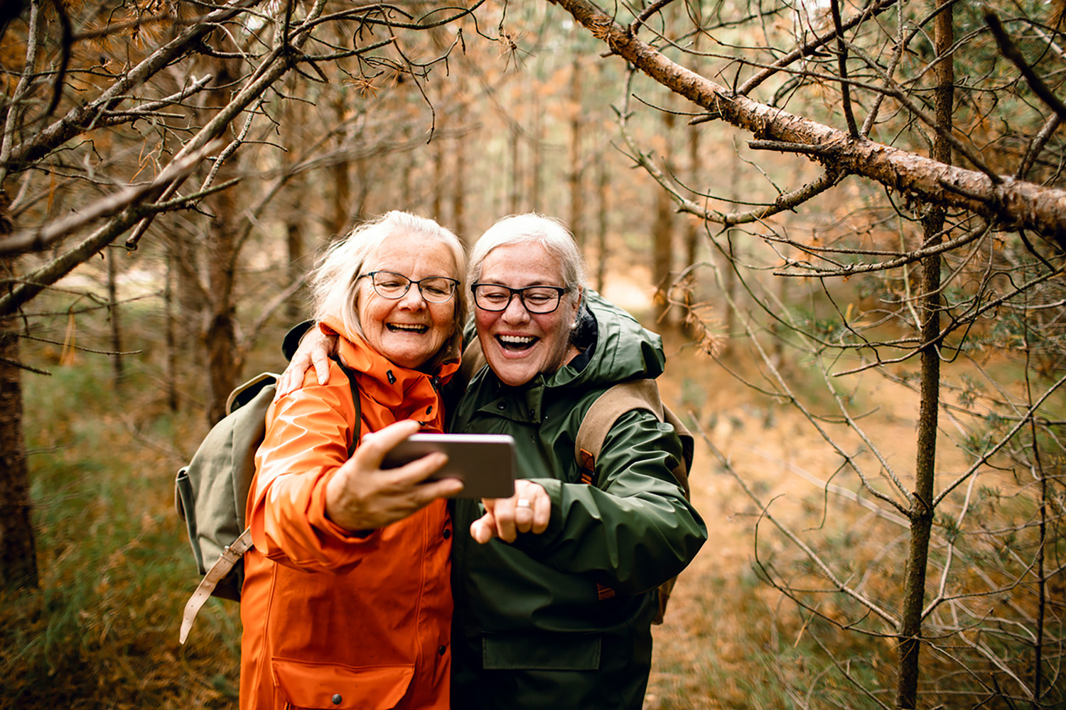 Two senior women, smiling and taking a selfie in the forrest