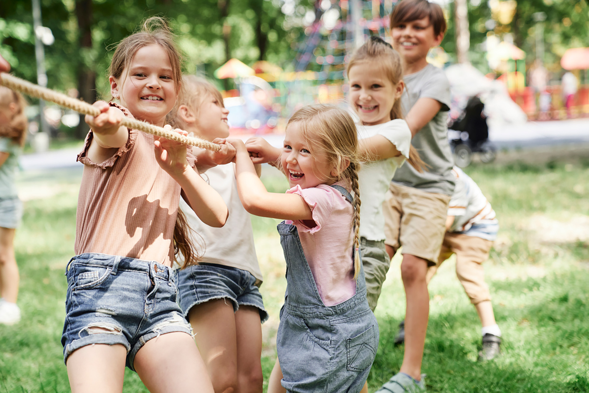 A group of kids, pulling a rope in a park