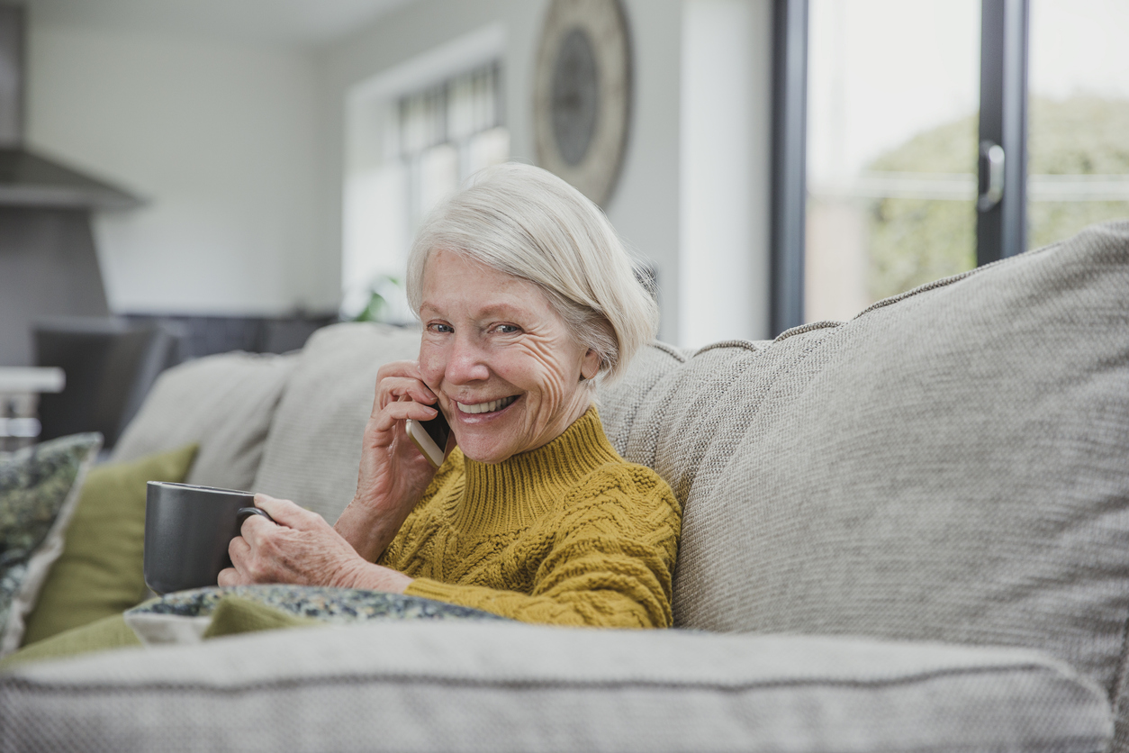 Senior woman sitting in a sofa, enjoying a phonecall and a cup of tea