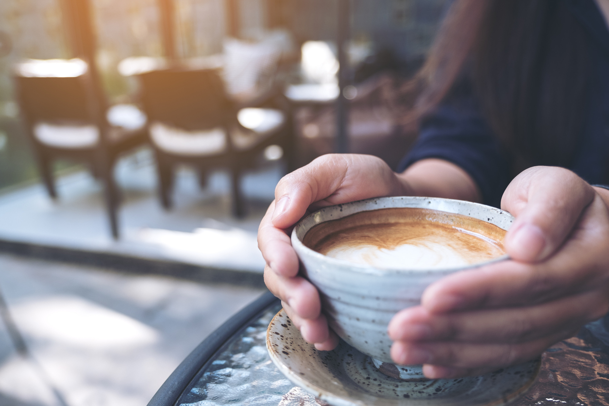 Close-up of hands holding a cup of hot coffee on glass table in a cafe