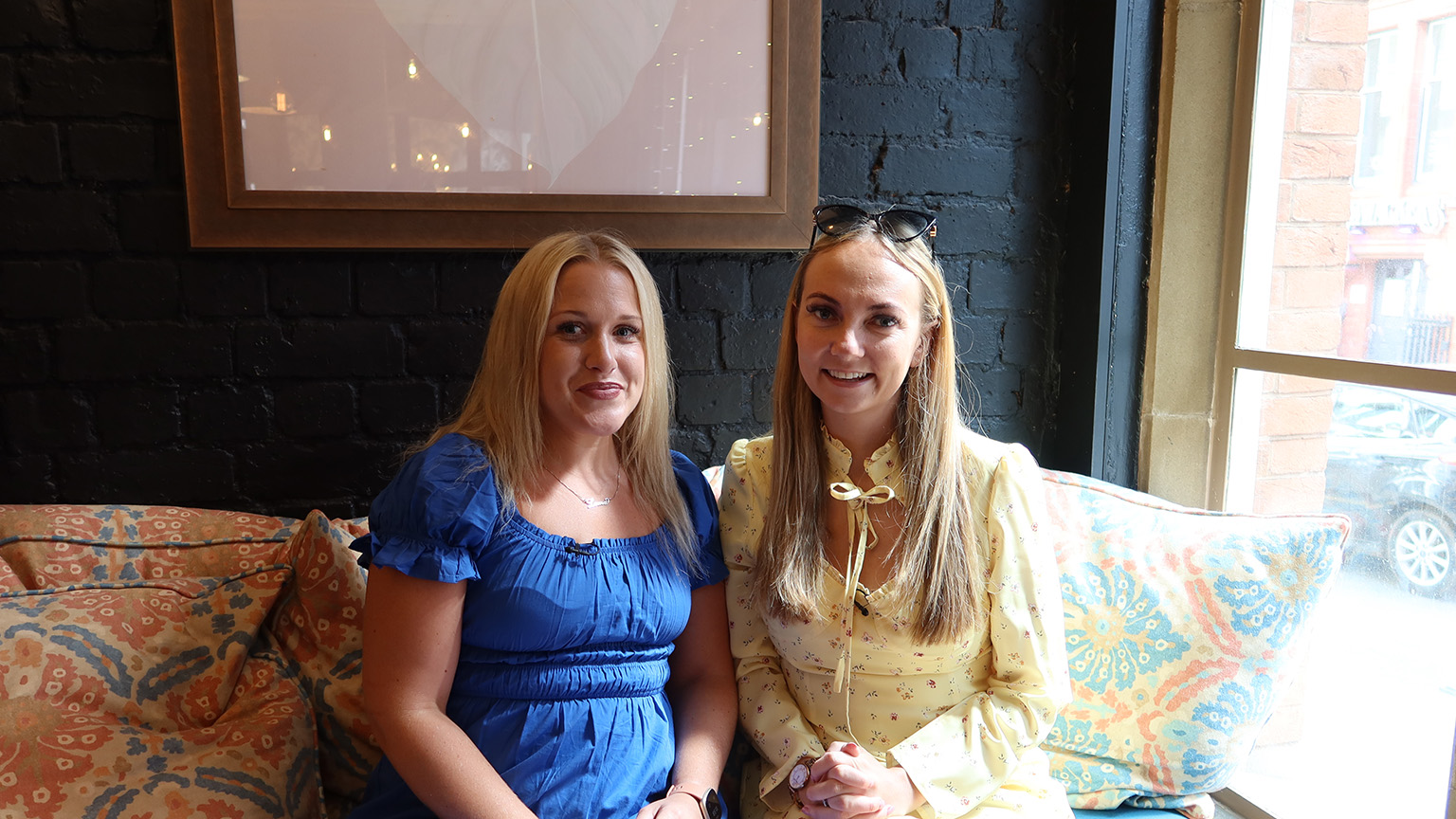 Two girls sitting at a cafe, smiling at the camera