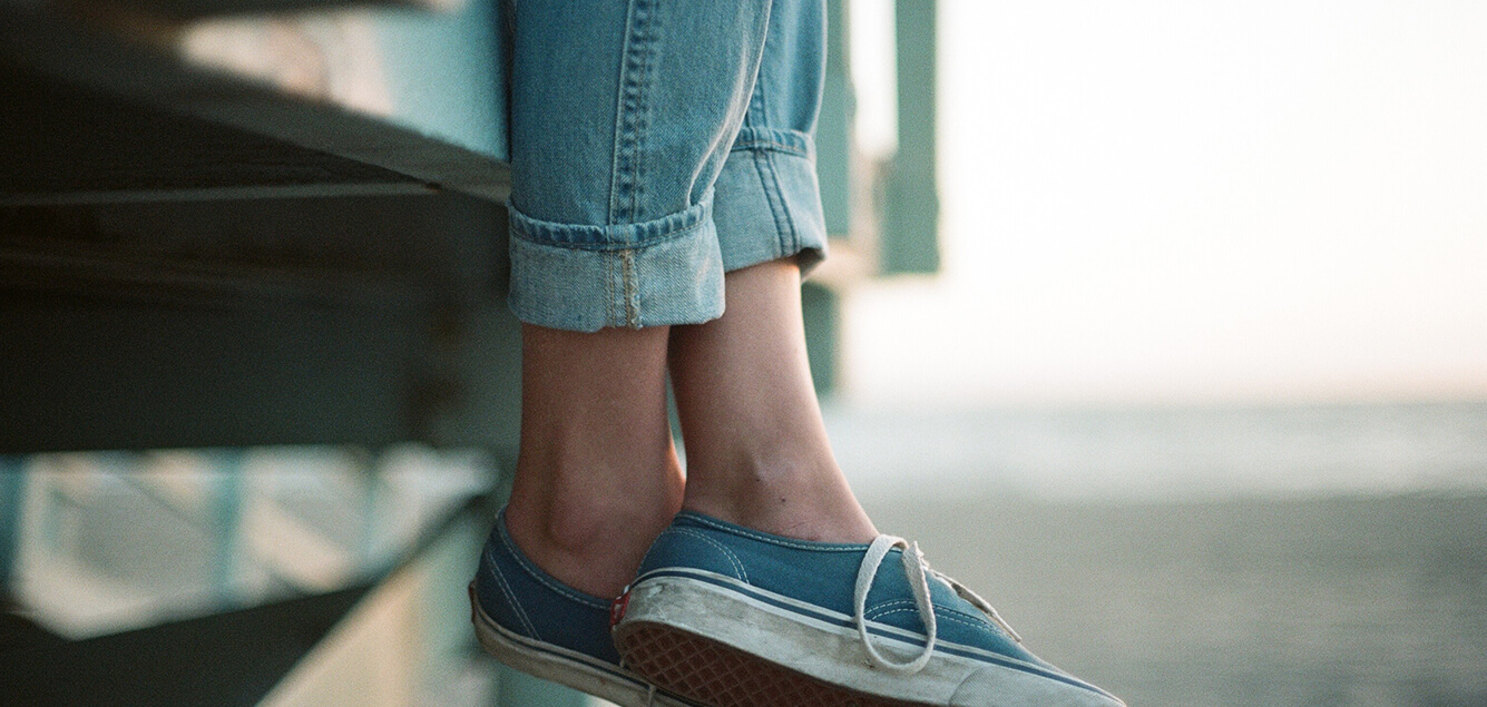 Photo of someone's relaxed feet with shoes sitting on the pier.
